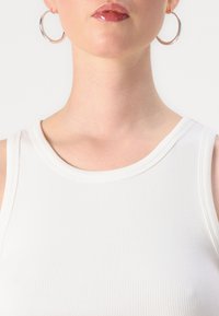 Hvit ribbet tank topp med rund hals og glatt tekstur. Store sølvfargede hoops øredobber komplementerer antrekket.