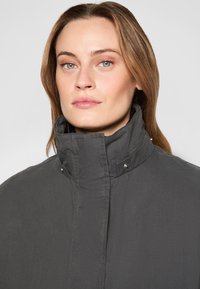 Gray high-collar jacket featuring button accents, a smooth texture, and a fitted design. The fabric appears lightweight and casual.