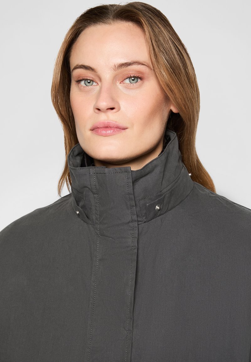 Graue Jacke mit hohem Kragen, die mit Knopfdetails versehen ist, einer glatten Textur und einem taillierten Schnitt. Der Stoff wirkt leicht und lässig.