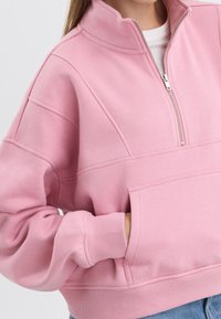 Roze zip-up sweatshirt met een hoge kraag, ribgebreide manchetten en een voorzak. Zacht materiaal en een relaxte pasvorm met naaddetails.