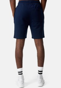 Marineblauwe katoenen shorts met een elastische tailleband en een achterzak, met een gladde textuur en een knielange snit. Witte sokken met zwarte strepen.