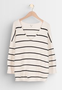 Pull blanc en maille côtelée avec des rayures horizontales noires, col en V, coupe ample et coutures d'épaule tombantes, suspendu à un cintre en bois.