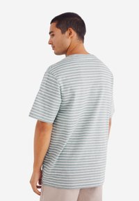 Šedý a bílý pruhovaný tričko s krátkým rukávem, uvolněného střihu a kulatým výstřihem. Hladká látka, viditelné švy a jemná textura.