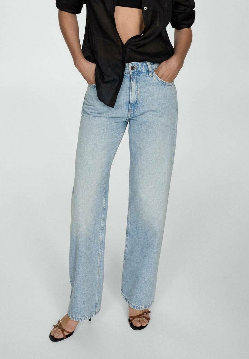 Jeans de pernera ancha de un azul claro, hechos de denim, con una cintura alta, diseño clásico de cinco bolsillos y detalles de dobladillo sin terminar. Combinados con sandalias negras.