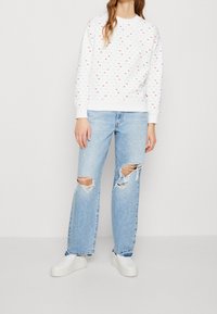 Felpa bianca con pois multicolori, colletto rotondo, polsini a costine, abbinata a jeans strappati azzurri e scarpe slip-on bianche.