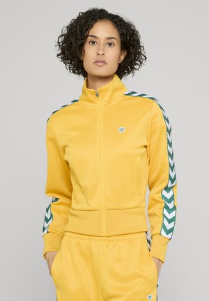 Żółta kurtka na zamek błyskawiczny z wysokim kołnierzem, z zielono-białymi paskami w kształcie szewronu na rękawach oraz małym logo na piersi.