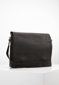 Borsa a tracolla in pelle nera con chiusura a pattina, tracolla regolabile e superficie liscia. Presenta cuciture minime e una piccola etichetta con logo.