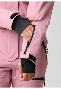Pink outerwear with black accents, featuring a zipper on the sleeve, Velcro closures, and a smooth texture. Notable stitching detail visible.