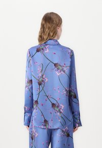 Πουκάμισο με μακριά μανίκια από λεία μπλε ύφασμα, με λουλουδάτο μοτίβο σε ροζ και πράσινες αποχρώσεις, και κλασική λεπτομέρεια γιακά.