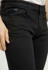 Czarne dżinsy o slim fit, z kieszenią z przodu, przeszyciami i suwakowym zapięciem. Gładka tekstura z delikatnym połyskiem.