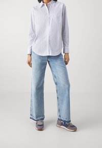 Pruhované tričko s dlouhým rukávem v bílé a modré barvě, doplněné o světle modré džíny s širokými nohavicemi. Obuv má kombinaci modré, šedé a oranžové barvy.