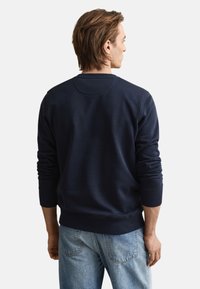 Mørkeblå sweatshirt med rund halsudskæring, ribstrikkede manchetter og kant. Trøjen har en glat, blød tekstur og løs pasform. Bruges med lyse jeans.