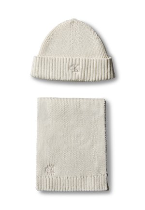 Ensemble bonnet d'hiver en maille crème et écharpe assortie avec bords côtelés et petit logo brodé sur chaque pièce sur fond blanc.