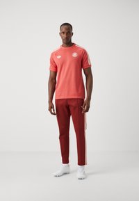 Röd atletisk t-shirt med vita detaljer, med rund hals och logotyp. Matchas med vinröda träningsbyxor och vita sportskor.