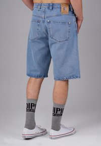 Faded blue denim shorts with a straight leg cut, five pockets, and a leather patch on the waistband. Paired with gray socks and white sneakers.