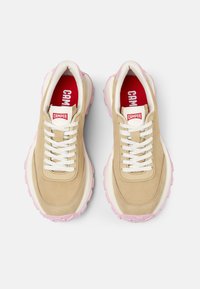 Beige suede sneakers with white laces, pink rubber soles, and red insoles. Features a logo label on the tongue. Rounded toe design.