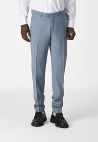 Pantalons bleu clair avec une texture lisse, présentant un design à l'avant plat, des passants de ceinture et une coupe ajustée. Associés à des chaussures noires à enfiler.