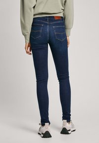 Jeans ajustados de denim azul oscuro con una textura suave. Presentan una cintura de altura media, detalles de costura y dos bolsillos traseros.