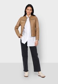 Veste en cuir tan avec une fermeture éclair à l'avant, deux poches poitrine et une coupe ajustée. Associée à une chemise blanche, un pantalon sombre et des baskets claires.