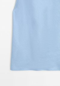 Tessuto azzurro chiaro con leggera trama, che mostra l'orlo inferiore di un capo d'abbigliamento su sfondo bianco.