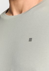 Lichtgroen T-shirt met korte mouwen, gemaakt van zachte stof, met een ronde hals en een klein, zwart gestreept logo op de borst.