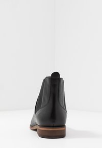Černá kotníková bota z kůže s elastickými bočními panely, kulatou špičkou a hnědým vrstveným podpatkem. Hladká textura s minimálními švy.