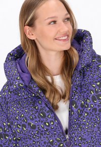 Lila Pufferjacke mit schwarzem und neongrünem Leopardenmuster. Verfügt über einen hohen Kragen, einen Reißverschluss und eine weiche Textur.