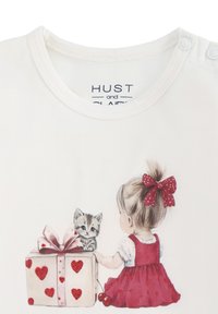 Maglietta bianca a maniche corte con un'illustrazione stampata di una ragazza in un vestito rosso, una scatola regalo con cuori e un gattino a righe.