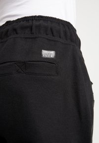 Zwarte sweatpants met elastische tailleband, voorzien van een klein merklabel dat op de achterzak is genaaid en een gestructureerde stofoppervlak.