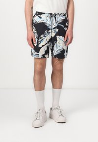 Costumi da bagno neri con motivo tropicale di foglie bianche e azzurro chiaro, vita elastica e tasche laterali, abbinati a sneaker bianche e calze.