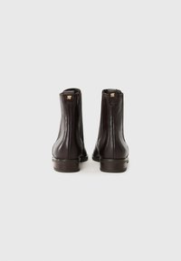 Bottes chevilles en cuir marron foncé avec une finition lisse, bout rond, petit talon et un logo discret à l'arrière. Design simple, sans embellissements.
