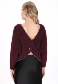 Bordeaux gebreide trui met een v-hals achteraan, met een wikkelontwerp en contrasterende bies langs de randen. Geconfigureerd met een losse pasvorm.