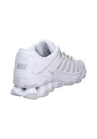 Le scarpe da corsa Nike bianche presentano una tomaia in mesh con sovrapposizioni in plastica, una suola ammortizzata e un design di ammortizzazione ad aria visibile sul tallone.