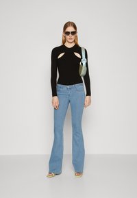 Top negro de manga larga con canalé y cortes, combinado con unos vaqueros acampanados de color azul claro. Accesorios en verde con sandalias y un bolso azul.