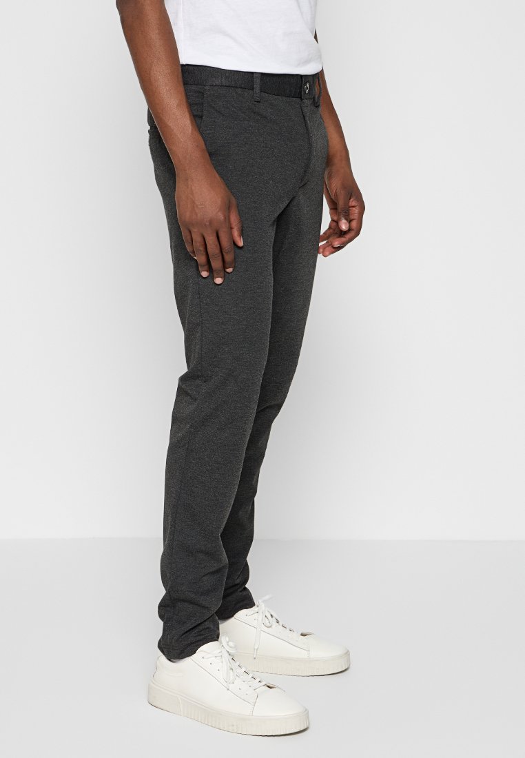 Szare dopasowane spodnie z miękkiego materiału, z zapięciem na guzik z przodu, szlufkami na pasek i kieszeniami bocznymi, w połączeniu z białymi trampkami.