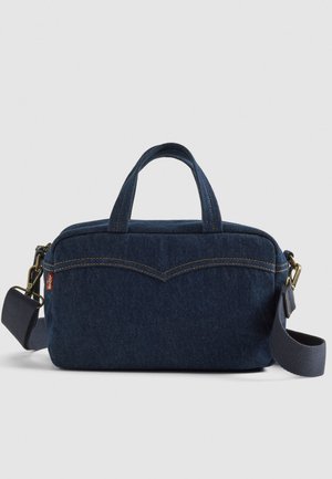 Denim tas, donkerblauw met twee korte handvatten en een afneembare schouderband. Heeft contrasterende stiksels en een gebogen ontwerp aan de voorkant.
