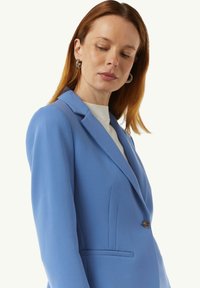 Lichtblauwe blazer van gladde stof, met een gesneden revers, sluiting met één knoop en zijzakken met een getailleerde pasvorm.