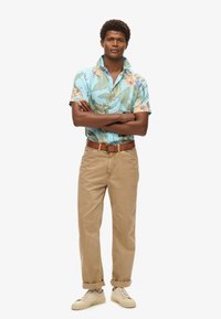 Camicia a maniche corte, azzurra con motivo floreale e foglie verdi, abbinata a pantaloni beige con risvolti e sneakers color crema. Inclusa cintura marrone.
