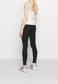 Svarta leggings med en sträckbar, åtsittande design, kombinerade med en vit ärmlös topp och flerfärgade sneakers. Minimalistisk stil.