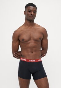 Fekete boxer alsónadrág rugalmas anyagból, piros Levi's logós derékpánttal, összeillesztett kialakítással és sima textúrával.