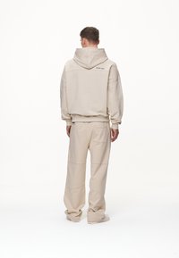 Felpa beige in pile con un ampio cappuccio e polsini a coste, abbinata a pantaloni coordinati con tasca laterale e vestibilità rilassata.