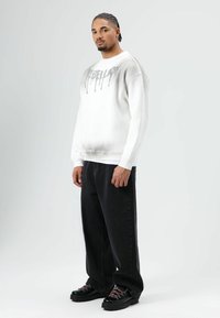 Witte sweatshirt met grijze gradient, "DIESEL" logo in druipende letters; gecombineerd met zwarte baggy jeans en zwarte schoenen met roze veters.