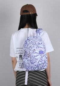 Purple patterned backpack with multiple zippered compartments, padded straps, and an ergonomic design. Worn on the back of a person.