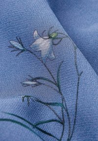 Tissu bleu texturé avec un imprimé botanique délicat comprenant de fines tiges et de petites fleurs blanches et vertes.