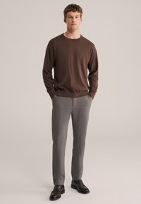 Barna hosszú ujjú pulóver kerek nyakkivágással, világosszürke mintás nadrággal és fekete bebújós cipővel kombinálva. Egyszerű, modern dizájn.