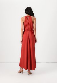 Vestido maxi em vermelho escuro com decote halter, cintura elástica e detalhe de recorte nas costas. Tecido suave e fluido cria uma silhueta suave.