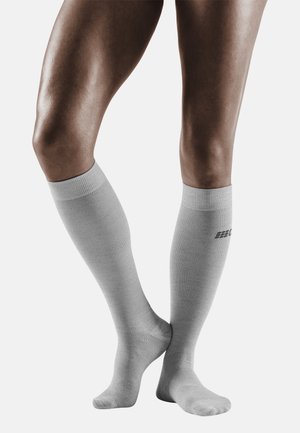 Graue knielange Socken, gerippte Textur, elastischer Bund, mit einem Logo-Akzent nahe dem oberen Rand. Die Socken sitzen enganliegend am Bein.