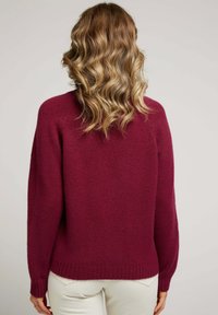 Pull en tricot bordeaux à coupe décontractée, encolure ronde, ourlet et poignets côtelés, texture douce et manches longues.