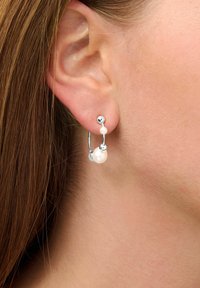 Orecchini a cerchio in argento con una finitura lucida, caratterizzati da due perle bianche e accenti sferici, indossati all'orecchio di un modello.