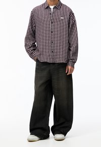 Camicia con bottoni a maniche lunghe in un motivo a quadri viola e bianco, abbinata a jeans neri larghi e sneaker bianche.